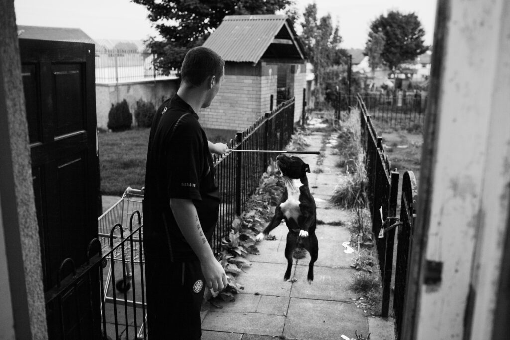 Peter holds out a stick as his dog jumps up to play in the back garden of his Easterhouse home.