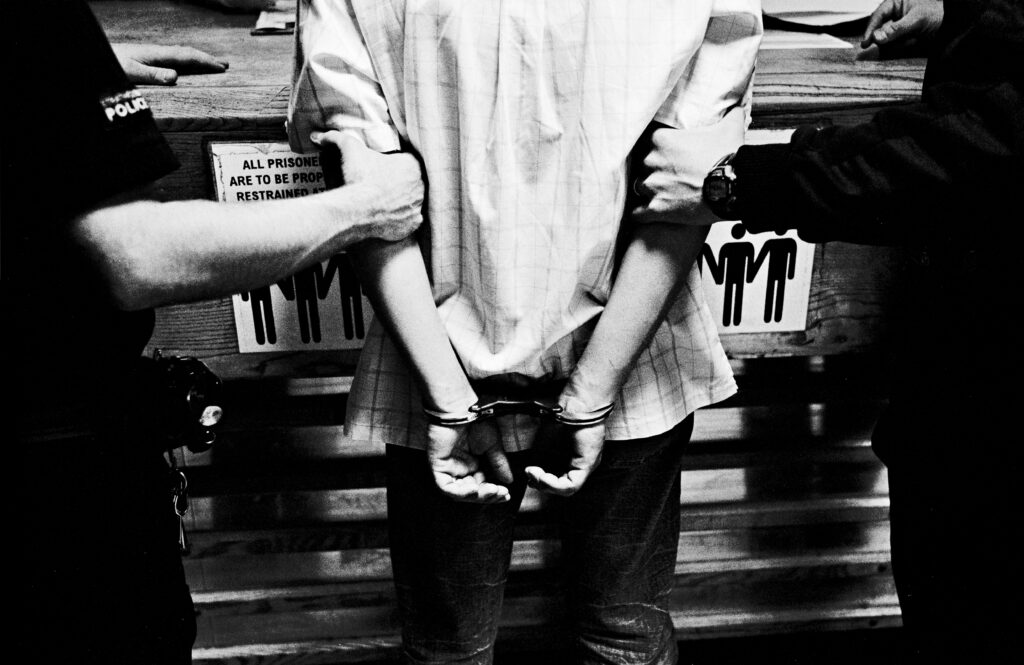 A young man in handcuffs at the booking desk in a police station in Glasgow after being arrested during a gang fight.